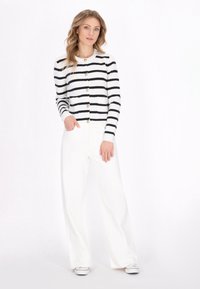 Black and white striped cardigan with gold buttons, paired with white wide-leg trousers and white sneakers, on a model against a light background.