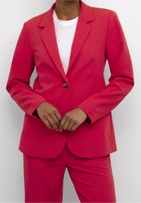 Fuchsia blazer met een enkele knoopsluiting, ingesneden revers en lange mouwen, gecombineerd met bijpassende broek en een wit shirt met ronde hals.