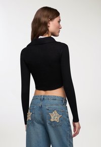 Maglione nero a coste corto con un ampio colletto, abbinato a jeans azzurri chiari con toppe a forma di stella leopardate sulle tasche posteriori.
