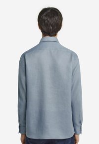 Ljusblå långärmad skjorta av strukturerad väv med spetsig krage och knappade ärmmuddar, med en avslappnad, lös passform.