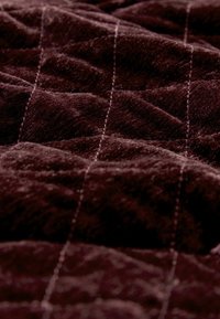 Mjuk, mörk burgundyröd textil med en mjuk yta, prydd med ett quiltat mönster och kontrasterande ljusa sömmar.