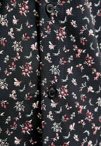 Tkanina w kwiatowy wzór w kolorze czarnym, z małymi różowymi i białymi kwiatkami. Zawiera szczegół z przodu na guziki z teksturowanym splotem.
