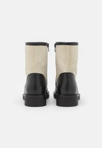 Botas de tornozelo em couro preto com painéis têxteis em bege, apresentando um fecho lateral com zip e uma sola grossa preta para maior estabilidade.