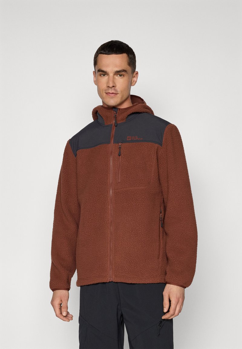 Veste en polaire de couleur rouille avec un panneau d'épaule noir et une capuche. Le tissu texturé comporte une fermeture éclair à l'avant et une poche poitrine avec fermeture éclair.