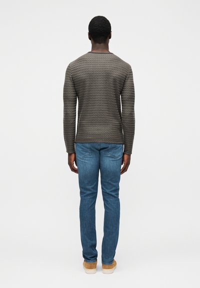 Camisola cinzenta com padrão em zigzag texturizado, combinada com jeans azuis e sapatos cor de caramelo, vista de costas.