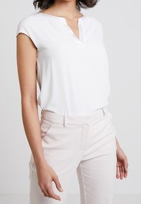 White short-sleeve blouse with a V-neck and smooth texture, paired with light pink tailored trousers featuring side pockets.