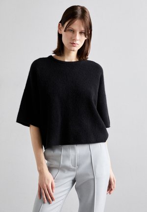 Pull noir à manches courtes en tissu doux et texturé avec une coupe décontractée. Assorti à un pantalon gris clair sur mesure.