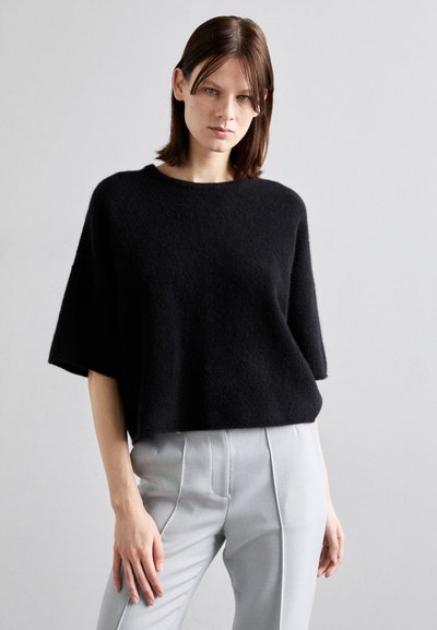 Pull noir à manches courtes en tissu doux et texturé avec une coupe décontractée. Assorti à un pantalon gris clair sur mesure.