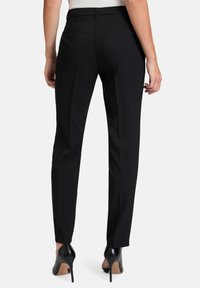 Čierne nohavice na mieru s úzkym strihom, vyrobené z hladkej tkaniny, so straight strihom a dvoma zadnými vreckami. V kombinácii s čiernymi vysokými podpätkami.