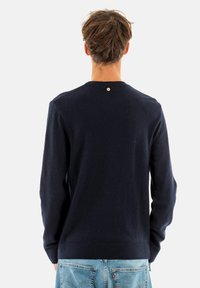 Maglione blu navy con scollatura rotonda, polsini e orlo a coste, e un piccolo dettaglio con bottone sul retro. Realizzato in un morbido tessuto testurizzato.