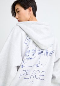 Hallikas ülikõrge kapuutsiga, millel on sinise värvi karikatuurikassi kujundus ja all sõna "RAHU". Pehme, puuvilla ja sünteetika segu kanga materjal.