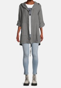 Veste à capuche en lin gris avec design à ouverture sur le devant, deux poches avant et cordon de serrage à l'ourlet, associée à un jean bleu clair et des bottines grises à lacets.