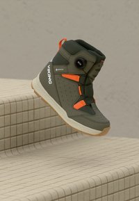 Botte viking en vert olive hautes avec des accents orange, semelle blanche, cadran BOA et matériau Gore-Tex, affichée en apesanteur au-dessus de marches carrelées.