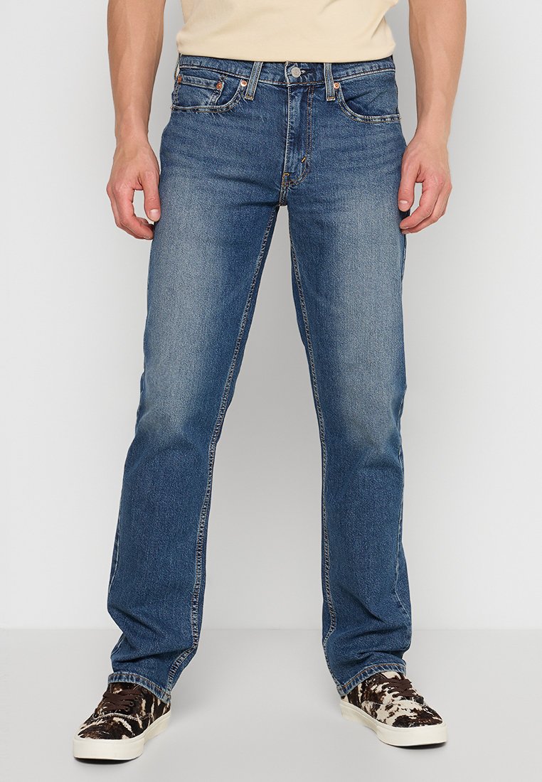 Blå denimjeans med rak ben-design, fem fickor, kopparstickningar och en lätt urblekt textur. Bärs med mönstrade sneakers.