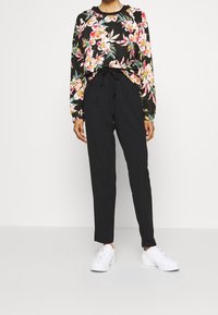 Zwart sweatshirt met bloemenpatroon en lange mouwen, gecombineerd met losse zwarte broek en witte sneakers. Casual outfit met een taille met trekkoord.