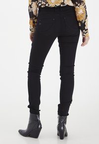 Jeans ajustados negros con una textura suave, con una cintura de altura media, diseño de cinco bolsillos y acentos de hardware mínimos.