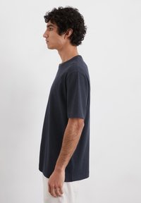 Marineblå bomulds t-shirt med rund halsudskæring, korte ærmer og en afslappet pasform, vist på en model i profil.