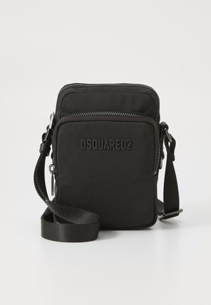 Sac bandoulière en nylon noir avec deux compartiments zippés, une sangle ajustable et un logo en relief sur le devant. Design compact et rectangulaire.