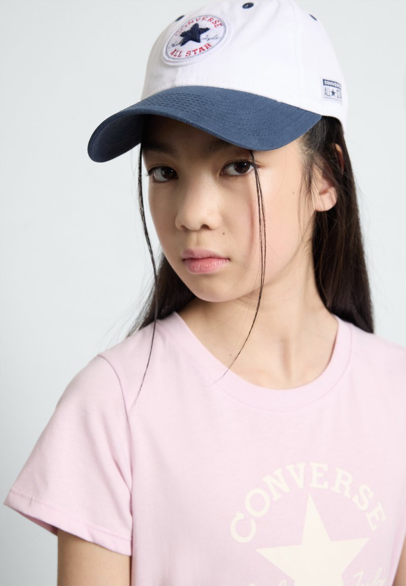 Hvid og navy baseballcap med et stjerne-logo, båret med en lyserød T-shirt med et stort stjerne grafik. Glat stofstruktur.