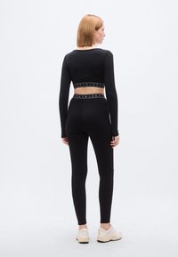 Μαύρο μακρυμάνικο τοπ και εφαρμοστά κολάν με λάστιχο μέσης με σήμανση. Ομαλή υφή, μίνιμαλ σχεδίαση και ουδέτερο φόντο.