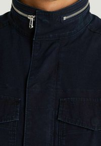 Navy blue jacket with a high collar, zipper closure, and two chest pockets. Made from a smooth material with subtle texture.