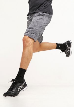 Personne portant un short gris, des chaussettes noires et des chaussures de course noires au milieu d'une foulée, avec une jambe tendue en avant et l’autre pliée derrière.