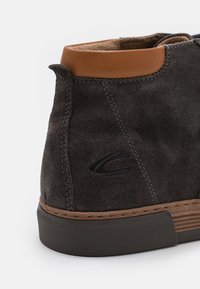 Graue Wildleder-Stiefelette mit einem braunen Lederbesatz, ausgestattet mit einer strukturierten Gummisohle und genähten Akzenten, einschließlich eines Logos.