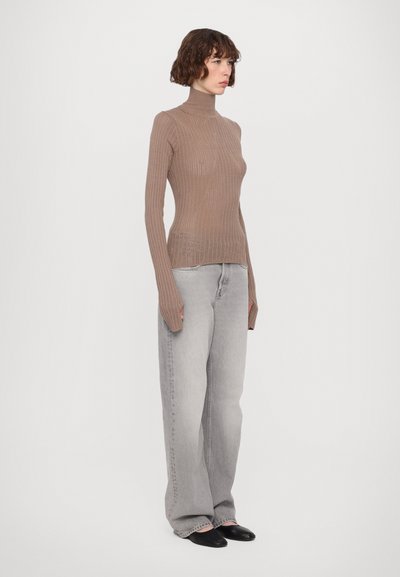 Ribbed turtleneck neule valoissa ruskeissa, valmistettu ohuesta materiaalista, yhdistettynä väljiin harmaisiin farkkuihin ja mustiin liukuviin kenkiin.