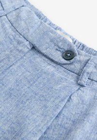 Světle modrá látka s texturovaným povrchem, obsahující elastický pas a černý knoflík, navržená pro pohodlí a snadné nošení.