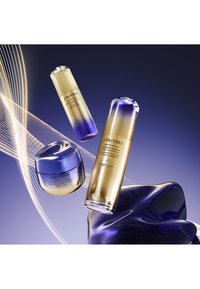 Tre Shiseido hudpleieprodukter: en rund blå krukke, en høy flaske med gyllen-til-blå gradient, og en kort sylindrisk flaske med lignende gradient.