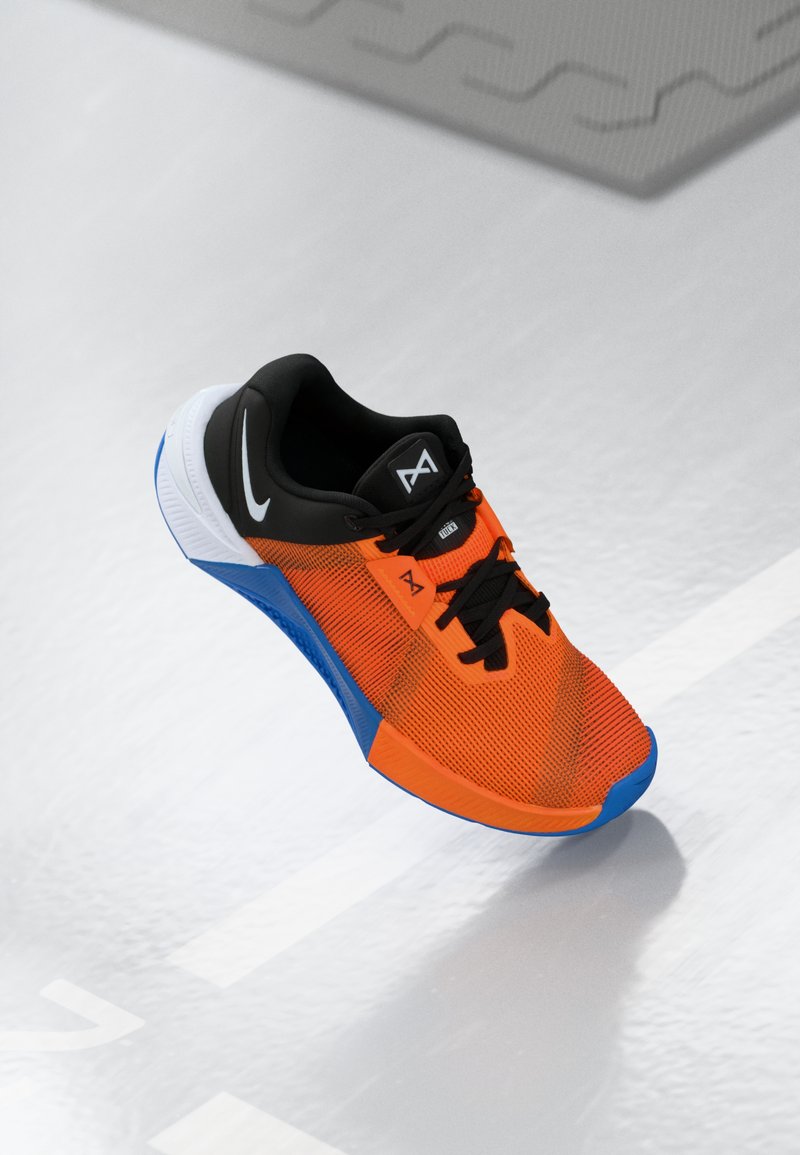 Sportsko med en orange mesh-overdel, sorte detaljer, blå sål og en detaljeret tekstur. Inkluderer sorte snørebånd og logo.