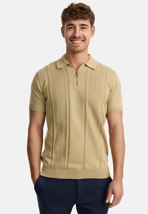 Polo shirt beige a maniche corte con colletto a zip, caratterizzato da rifiniture a costine e strisce verticali testurizzate. Indossato con pantaloni blu navy.