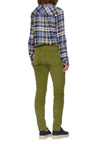 Groene corduroy broek met een getailleerde pasvorm, gecombineerd met een blauw en groen geruit shirt en donkere sneakers. Zichtbare achterzakken en textuurdetails.