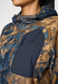Fleece pullover met een blauw en bruin gemarmerd patroon, voorzien van een zwarte textielzak en een verstelbare trekkoord op een hoge kraag.