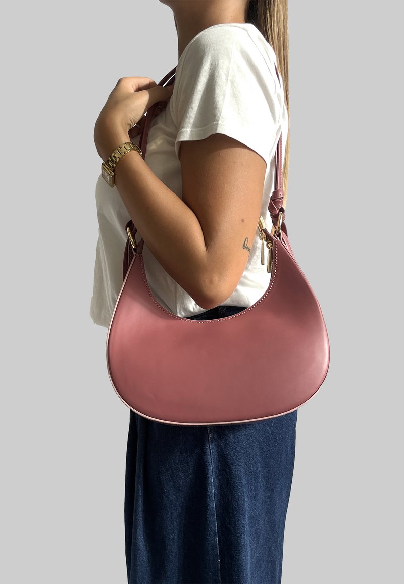 Borsa in pelle rosa con una forma curva a mezzaluna. Texture liscia, dettagli in hardware dorato e una sola tracolla.