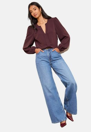 Mörk lila blus med V-ringning och puffärmar, kombinerad med högmidjade ljusblå vida jeans och bordeauxfärgade pumps med spetsig tå.