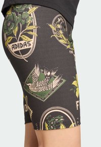 Bermudas pretas com um padrão floral e de pássaros em verde e bege, feitas de um tecido elástico com uma cintura elástica.