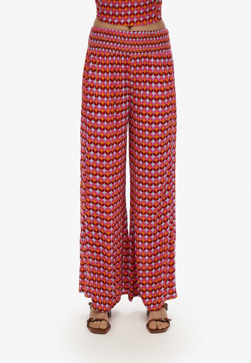 Pantalones de pierna ancha en un vibrante patrón geométrico rojo y púrpura, hechos de una tela ligera con una cintura elástica para mayor comodidad.