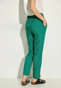 Grønne mønstrede bukser med elastisk talje, slim fit og sidelommer. Kombineret med sorte sandaler med korksål.