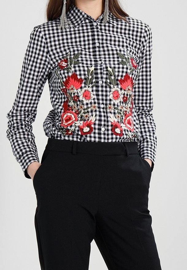 Randig skjorta i svart och vitt med röd blomsterbroderi på bröstet, knapprad, och långa ärmar. Bärs med svarta byxor.