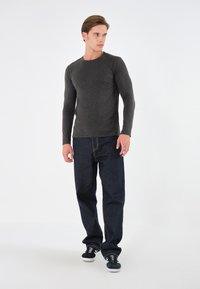 Houthakkershemd met lange mouwen in houtskoolkleur met een ronde hals, gecombineerd met loszittende donkerblauwe jeans. De outfit wordt compleet gemaakt met zwart-witte sneakers.