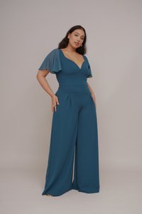 Türkisfarbener Jumpsuit mit tailliertem Oberteil, V-Ausschnitt und schwingenden Ärmeln. Besondere Merkmale sind weite Beine und Falten für zusätzlichen Textur und Bewegung.