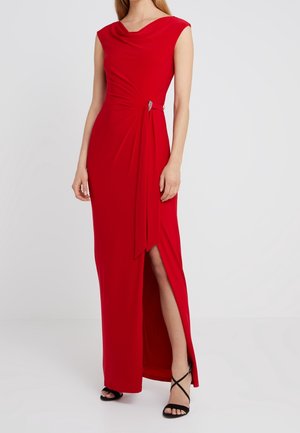 Sleeveless red evening gown with draped waist detail and side slit, worn with black strappy high-heeled sandals on a light background.