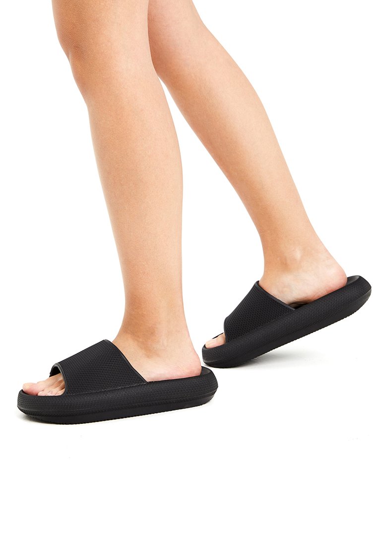 Black slide sandals with a textured upper, open toe design, and a thick rubber sole, featuring a slightly raised heel.