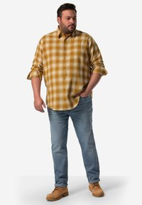 Camicia di flanella gialla e bianca a quadri con chiusura a bottoni, maniche arrotolate, abbinata a jeans azzurri chiari e stivali beige con lacci.