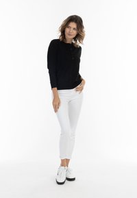 Cardigan nero con chiusura a bottoni, collo rotondo e maniche lunghe, abbinato a jeans bianchi a vestibilità slim e sneakers bianche con suole nere.