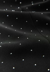 Tessuto nero con una superficie texture, adornato da piccole strass lucide sparse uniformemente sul materiale, che riflettono la luce.