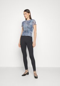 Top de denim azul claro con estampado y mangas cortas, con bordes deshilachados, combinado con leggings negros ajustados y zapatos planos con tiras negras.