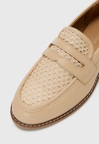 Beige Lederloafers mit einer gewebten Mesh-Front, flachem Absatz und einem dekorativen Riemen über dem Spann. Genähte Kantendetails.