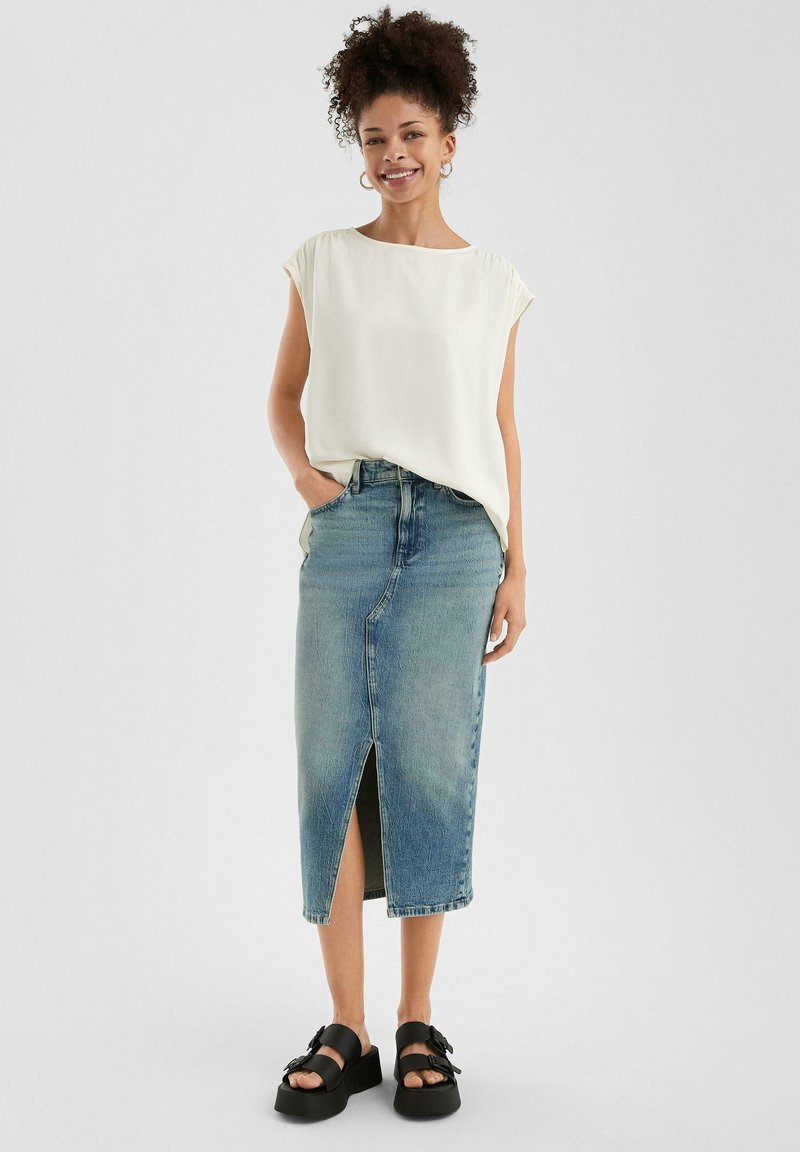 Bela, kratka majica s kratkimi rokavi, v kombinaciji z denim krilom do kolen svetlo modre barve, ki ima sprednji razporek. Obutev sestavljajo črne platforme sandali.